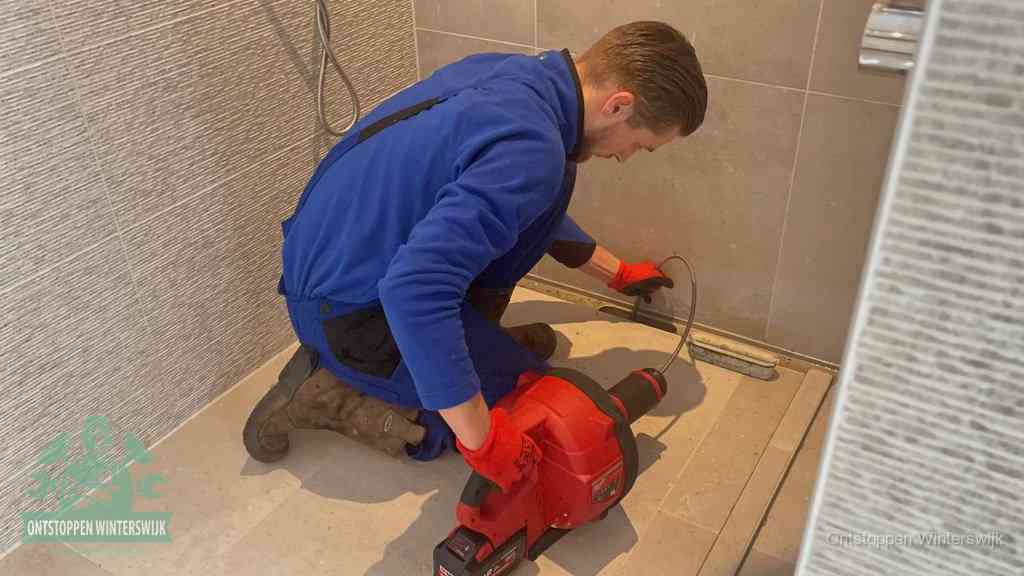 Een monteur ontstopt een langwerpige douchegoot met een elektrische veer, een doucheputje verstopt door haren en zeep in Winterswijk