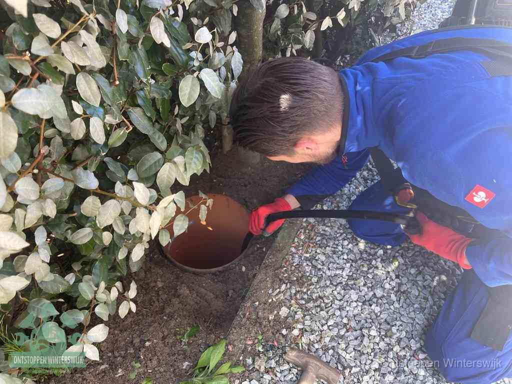 Een monteur voert een slang in een geopende rioolput in de tuin om het hoofdriool te ontstoppen in Winterswijk
