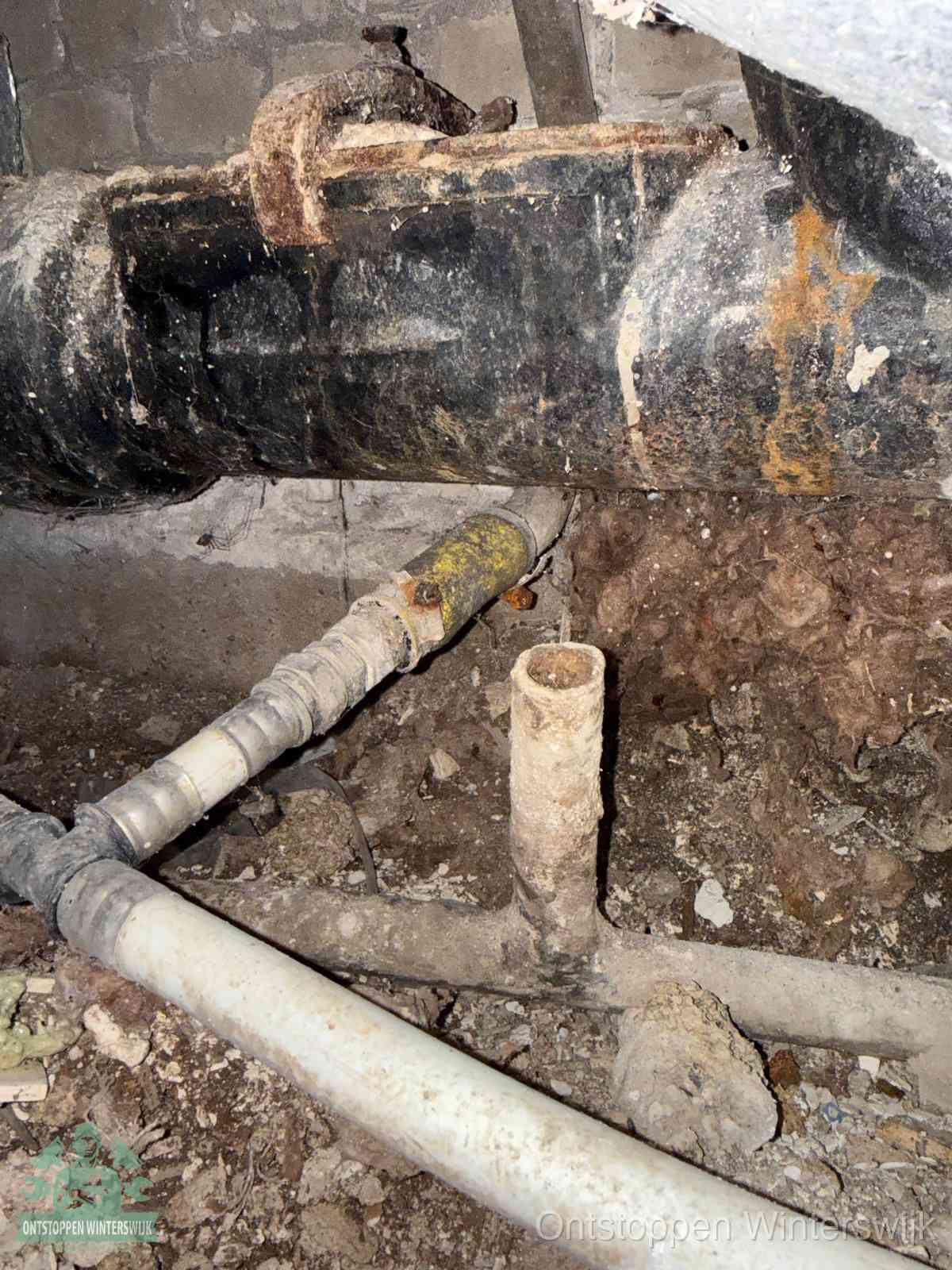 Een oude hoofdrioolbuis met roest- en kalkaanslag in een kruipruimte, oorzaak van terugkerende structurele rioolproblemen in Winterswijk